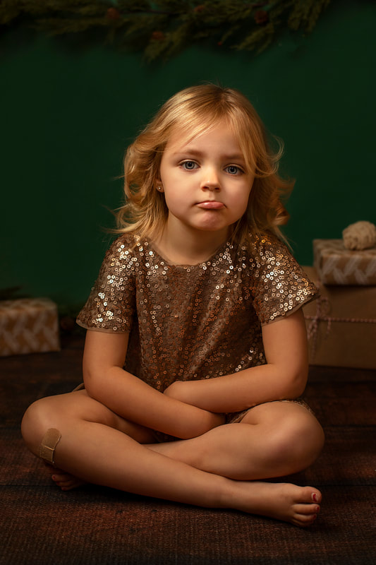 Photo of small girl with lip flipped in sparkling dress with dark green background. Gin Quist Photography
