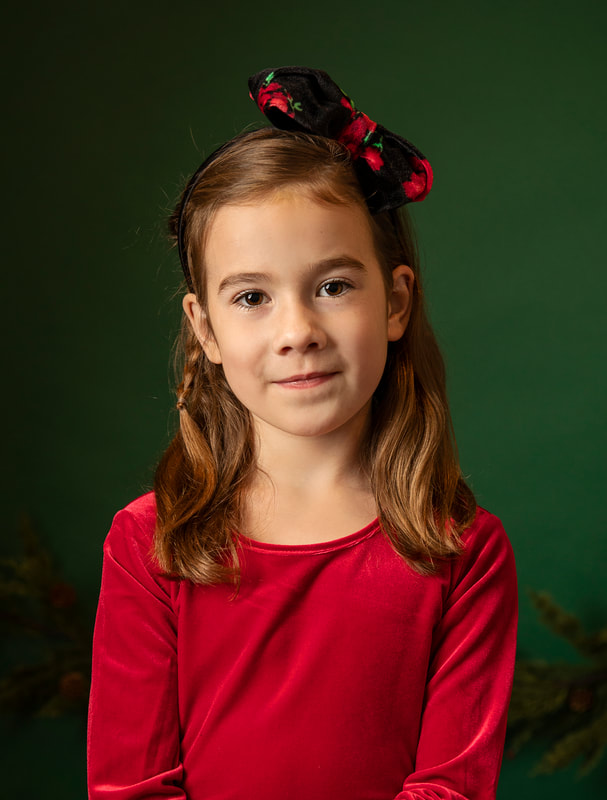 Young girl in red Christmas clothes sitting in studio set with green background. Gin Quist Photography