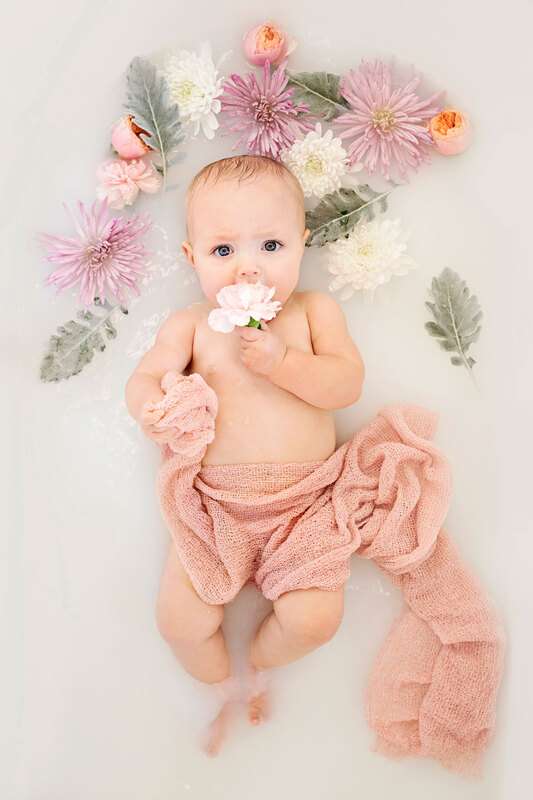 Baby in milk bath with flowers and pink fabric