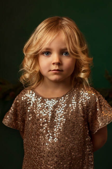 Photo of small girl in sparkling dress with dark green background. Gin Quist Photography