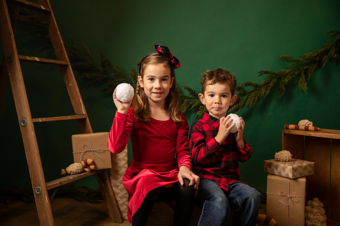 Boy and girl in red Christmas clothes sitting in studio set with green background. Gin Quist Photography