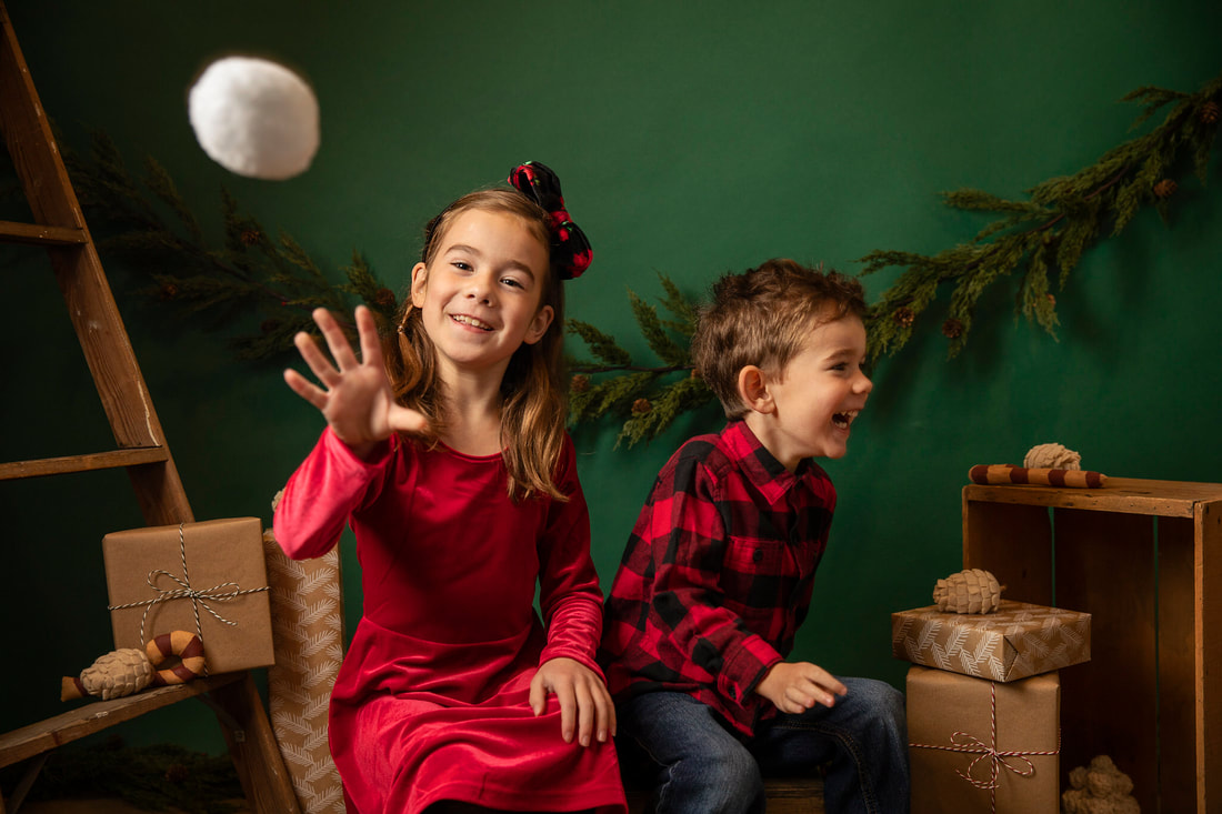 Boy and girl in red Christmas clothes sitting in studio set with green background. Gin Quist Photography